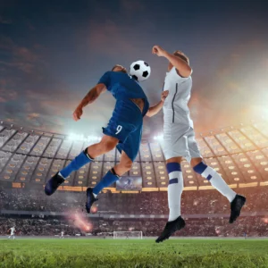 Two soccer players jumping to head the ball in a stadium.