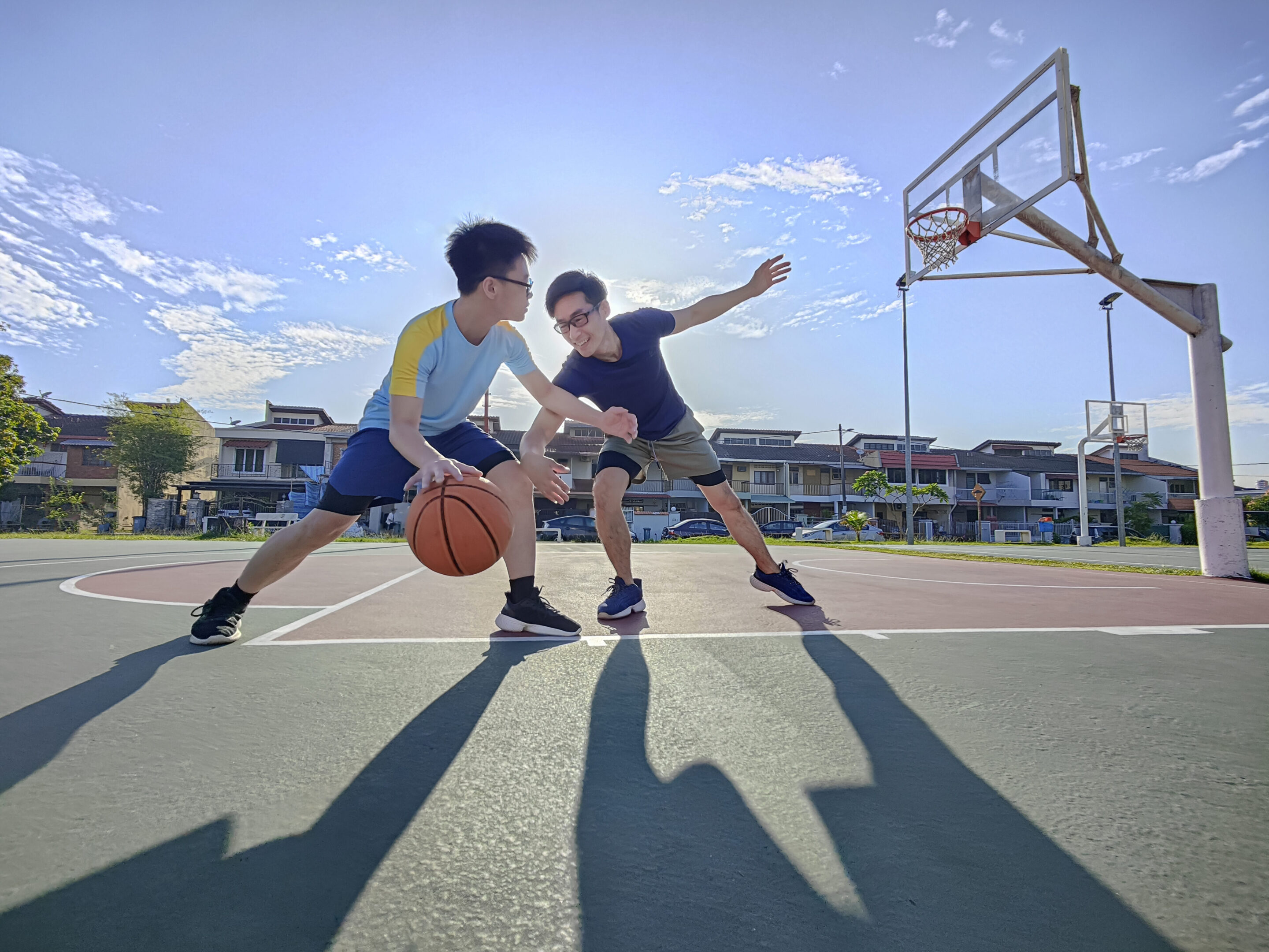 Two people playing basketball on outdoor court.